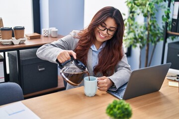 Young hispanic woman business worker pouring coffee on cup at office