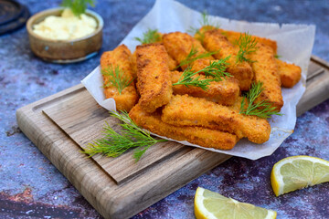 Close up of   Crispy breaded  deep fried fish fingers with breadcrumbs served  with remoulade sauce and  lemon Cod Fish Nuggets on rustic wood table background