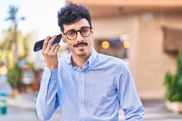 Young caucasian man smiling confident listening audio message by the smartphone at street