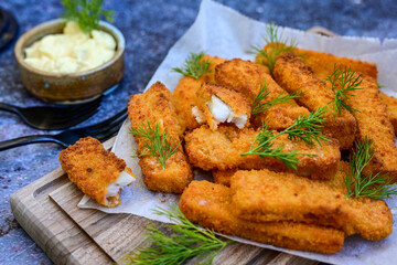 Close up of   Crispy breaded  deep fried fish fingers with breadcrumbs served  with remoulade sauce and  lemon Cod Fish Nuggets on rustic wood table background