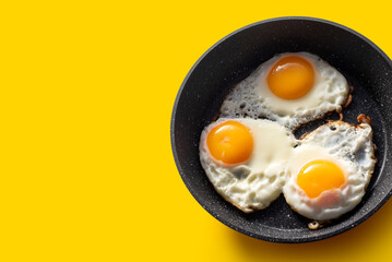 Frying pan with scrambled eggs from 3 eggs on a yellow background