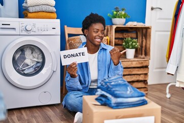 African american woman donating clothes pointing thumb up to the side smiling happy with open mouth