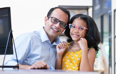 Indian cute little daughter and father are choosing appropriate eyeglasses for children in...