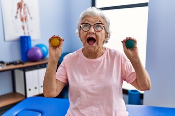 Senior woman with grey hair holding hands strength balls angry and mad screaming frustrated and furious, shouting with anger looking up.
