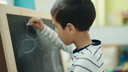 Adorable hispanic boy preschool student drawing on blackboard at kindergarten