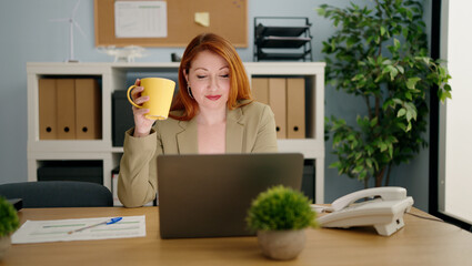 Young redhead woman business worker drinking coffee at office