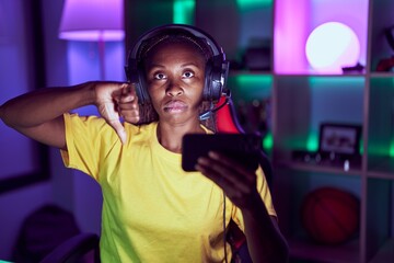 African american woman playing video games with smartphone with angry face, negative sign showing dislike with thumbs down, rejection concept