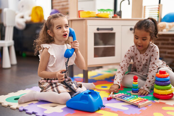 Two kids playing with telephone toy using xylophone sitting on floor at kindergarten