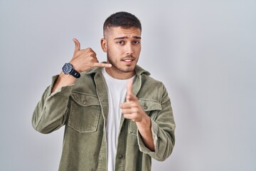 Young hispanic man standing over isolated background smiling doing talking on the telephone gesture...