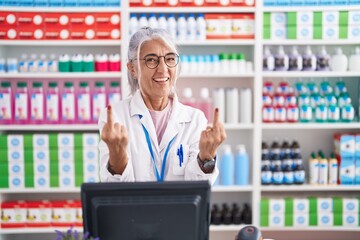 Middle age woman with tattoos working at pharmacy drugstore showing middle finger doing fuck you...