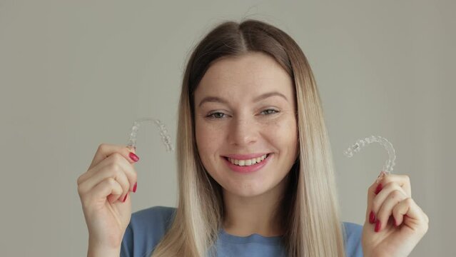 Cheerful woman holding transparent mouthguards for bite correction in clinic. A girl with a beautiful snow-white smile uses silicone braces