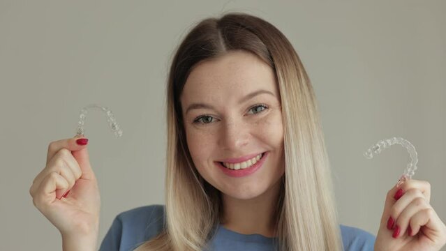 The woman is smiling and holding a transparent plastic aligner for bite correction