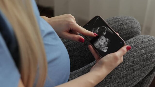Female waiting her baby, Pregnant woman looking her ultrasound scan photo on Smartphone. Concept of pregnancy, Maternity prenatal care.