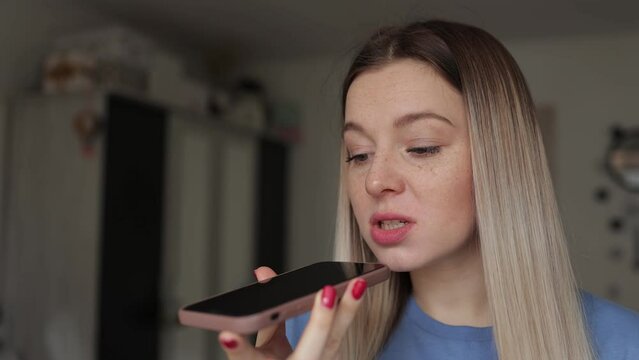 Internet communication. Young talkative smiling woman recording audio message on smartphone, telling news at home, free space