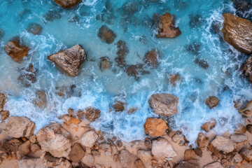 Aerial view of blue sea with waves, rocks and stones in clear water, rocky beach at sunny day in summer. Sardinia island, Italy. Beautiful seascape with sea coast, stones in azure water. Drone view