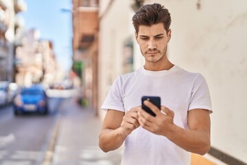 Young hispanic man using smartphone with serious expression at park