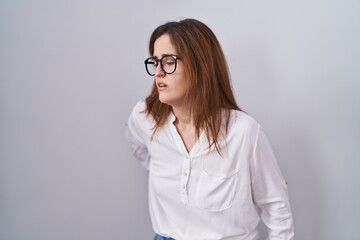 Brunette woman standing over white isolated background suffering of backache, touching back with hand, muscular pain