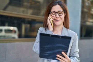 Young woman business worker talking on smartphone reading document at street