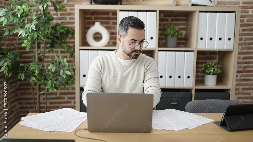 Sticker young hispanic man business worker using laptop reading document at office