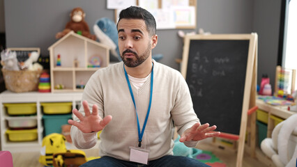 Young hispanic man preschool teacher asking for silence at kindergarten