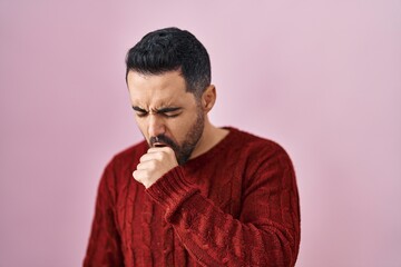Fototapeta na wymiar Young hispanic man with beard wearing casual sweater over pink background feeling unwell and coughing as symptom for cold or bronchitis. health care concept.