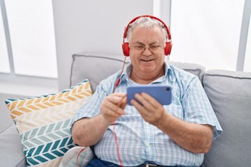 Middle age grey-haired man watching video on smartphone sitting on sofa at home