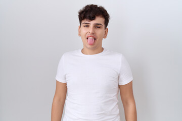 Young non binary man wearing casual white t shirt sticking tongue out happy with funny expression. emotion concept.