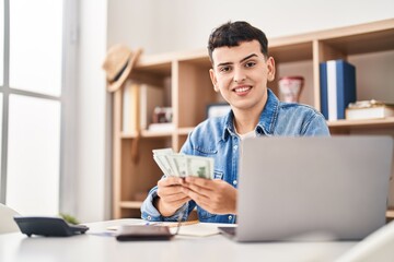 Young non binary man sitting on table counting dollars at home