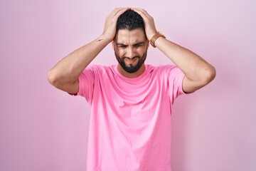 Fototapeta na wymiar Hispanic young man standing over pink background suffering from headache desperate and stressed because pain and migraine. hands on head.