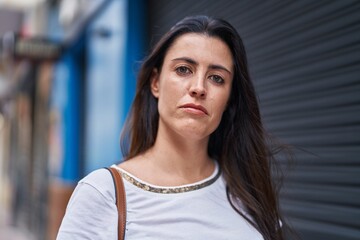 Young beautiful hispanic woman standing with serious expression at street