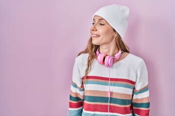 Young blonde woman standing over pink background looking away to side with smile on face, natural expression. laughing confident.