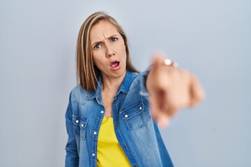 Young blonde woman standing over blue background pointing displeased and frustrated to the camera,...