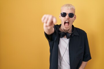 Obraz premium Young caucasian man wearing sunglasses standing over yellow background pointing displeased and frustrated to the camera, angry and furious with you