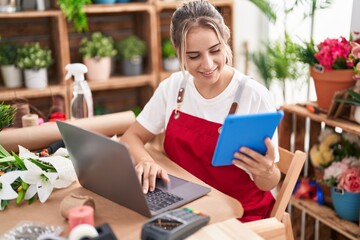 Young blonde woman florist smiling confident using laptop and touchpad at flower shop