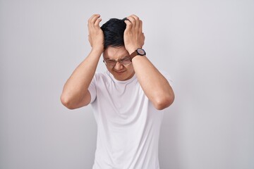 Young asian man standing over white background suffering from headache desperate and stressed because pain and migraine. hands on head.