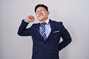 Young asian man wearing business suit and tie stretching back, tired and relaxed, sleepy and yawning for early morning