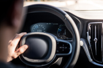 Detail of a man holding the steering wheel while driving calmly, when the digital speedometer shows...