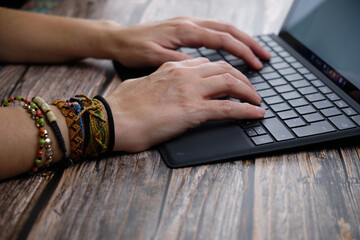 Close-up of a woman's hands working with a laptop on a wooden table.
