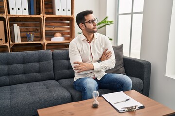 Young hispanic man with beard working at consultation office looking to the side with arms crossed convinced and confident