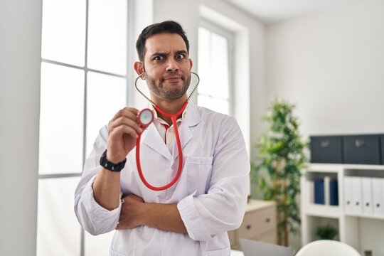 Young hispanic doctor man with beard holding stethoscope auscultating skeptic and nervous, frowning upset because of problem. negative person.
