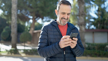 Fototapeta premium Middle age man smiling confident using smartphone at park