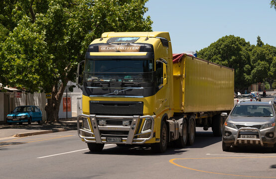 Western Cape, South Africa. 2023.  Yellow painted truck and trailer passing a car through the Western Cape area.