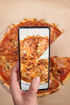 Woman photographing delicious pizza with mobile phone, smartphone to post to social networks, messenger. Vertical Orientation