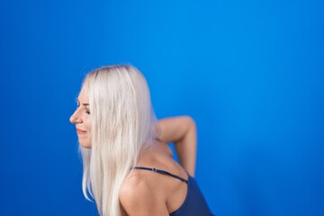 Fototapeta premium Caucasian woman standing over blue background suffering of backache, touching back with hand, muscular pain