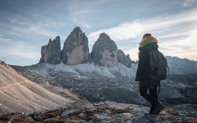 Woman with backpack with her back to the mountain peaks of the Tre Cime di Lavaredo trekking in Dolomites, Italy
