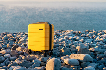 Yellow Suitcase with an orange scarf on the seaside against the sea. Travel concept.