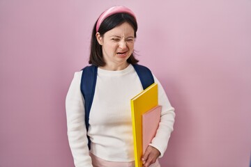 Woman with down syndrome wearing student backpack and holding books winking looking at the camera with sexy expression, cheerful and happy face.