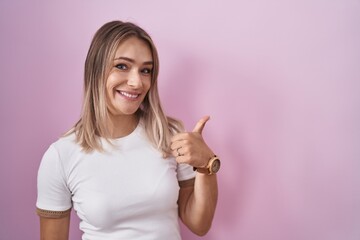 Blonde caucasian woman standing over pink background doing happy thumbs up gesture with hand....