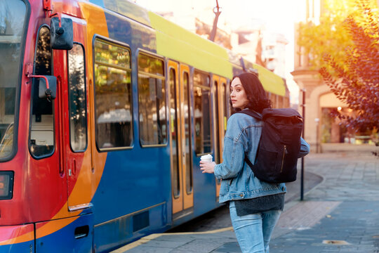 a young smiling woman in a denim jacket drinking coffee and  waiting for a tram at the stop Lifestyle photo