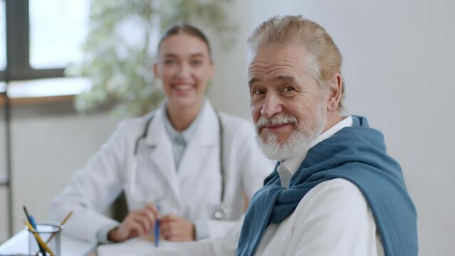 Aging and professional healthcare. Close up portrait of cheerful senior man patient sitting on consultation at clinic